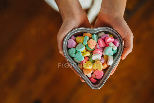 Overhead of child's hands holding candy hearts in heart dish — Stock Photo
