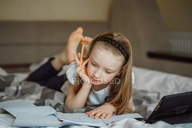 Menina deitada na cama cercada por cadernos — Fotografia de Stock