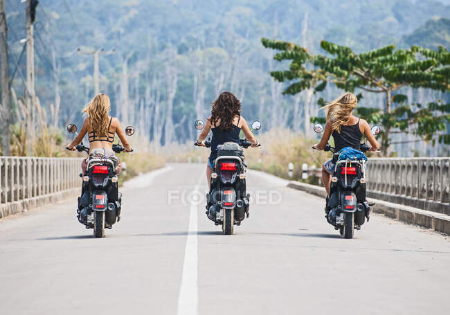 Three female friends riding scooters on highway in Laos — Stock Photo