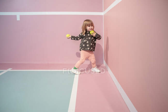 Маленька дівчинка розважається під час гри з тенісними м'ячами. Спорт і холодильник — стокове фото