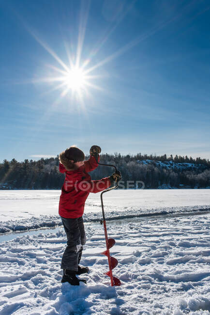 Jovem usando o trado para fazer um buraco no gelo em um dia ensolarado de inverno. — Fotografia de Stock
