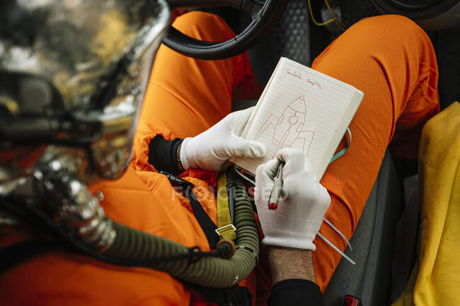 Man dressed as an astronaut draws a rocket on the notebook — Stock Photo