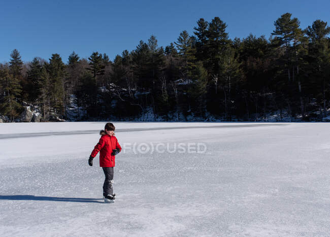 Jeune garçon patinant sur un lac gelé au Canada par une journée d'hiver ensoleillée. — Photo de stock
