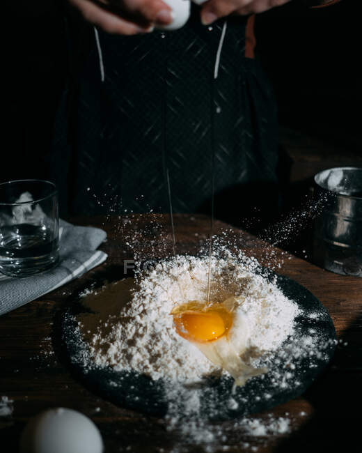 Frau fügt dem Mehl ein Ei hinzu — Stockfoto