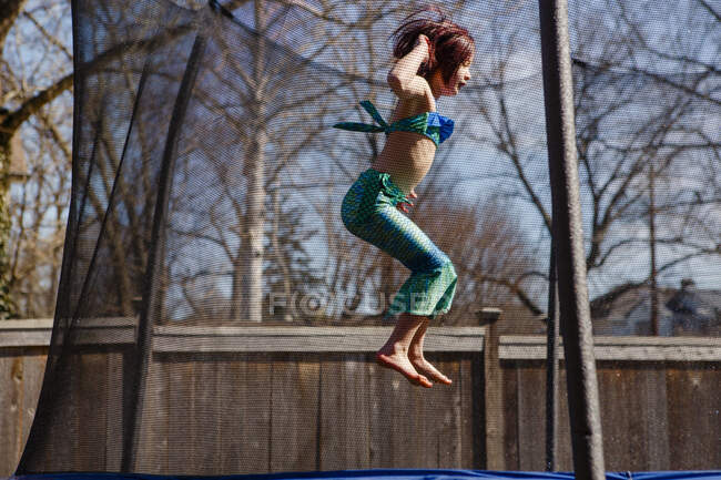 Маленька дівчинка в русалоньці стрибає босоніж на батуті — стокове фото