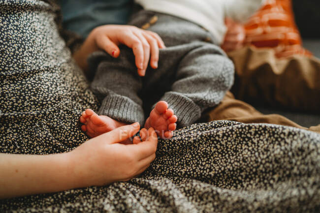Close up of older child holding newborn baby's feet at home — Stock Photo