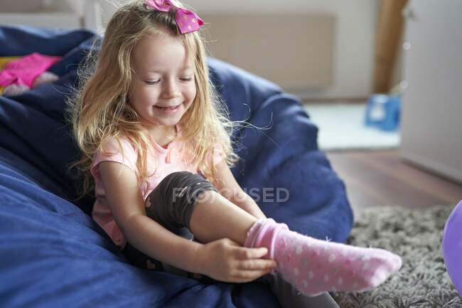 Щаслива маленька дівчинка сидить у сумці і одягає рожеві шкарпетки — стокове фото