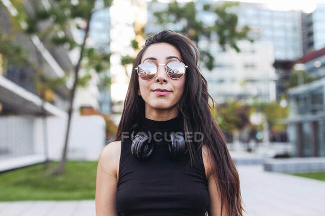 Eine junge schöne Frau mit langen lockigen Haaren in einem schwarzen Kleid und einem weißen T-Shirt und Sonnenbrille — Stockfoto