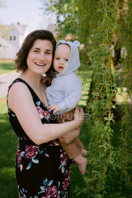 Мать и младенец сын улыбаются и играют в переднем дворе весной — стоковое фото