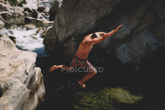 Junge in bunter Badehose springt von Klippe in schönen Fluss — Stockfoto