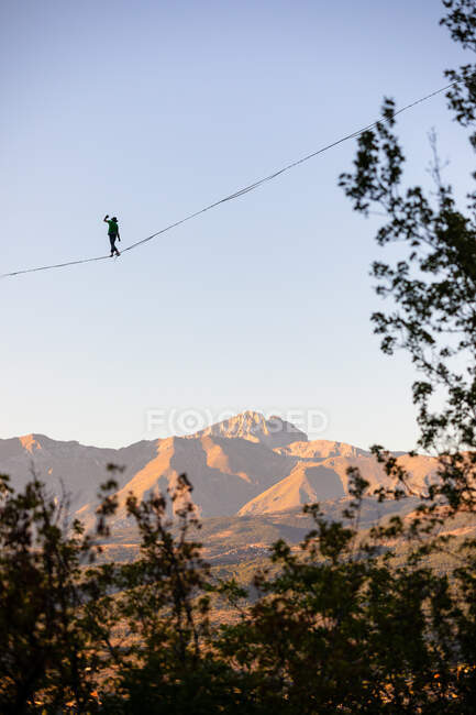 Slackliner walking over Gran Sasso with trees in the foreground — Stock Photo