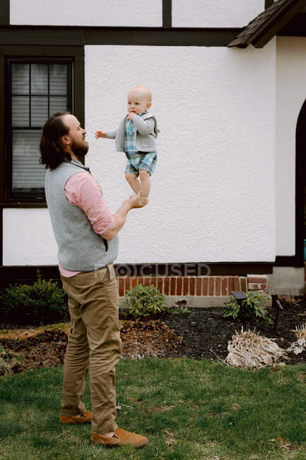 Divertido papá jugando con el bebé confundido hijo en el patio delantero en primavera - foto de stock