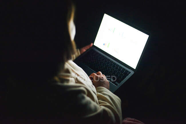 Mujer anónima trabajando en el ordenador portátil por la noche - foto de stock
