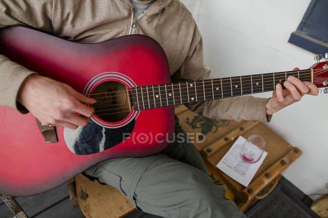 Primo piano di un uomo che suona una chitarra acustica rossa con un bicchiere di vino vuoto — Foto stock