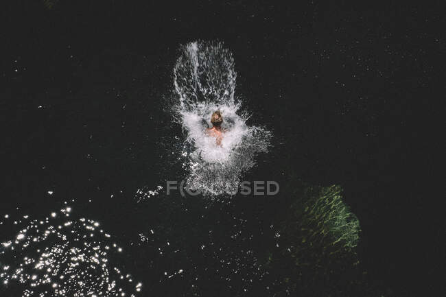Loira menino pula e terras em uma piscina escura Criando grande respingo — Fotografia de Stock