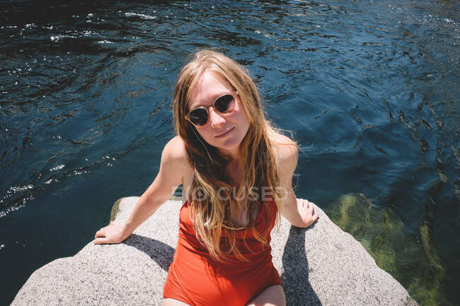 Loira em um terno vermelho e óculos de sol banhos de sol em uma tarde de verão — Fotografia de Stock