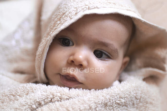 Un beau bébé roulé dans une serviette regardant autour dans la baignoire — Photo de stock