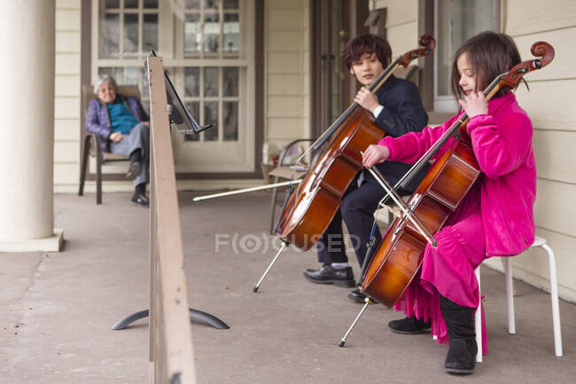 A los niños cumplen el violonchelo para el vecino mayor en el porche delantero - foto de stock