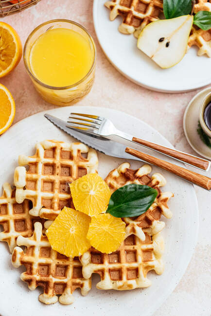 Homemade waffles on a light pink background. orange juice. fruit. — Stock Photo