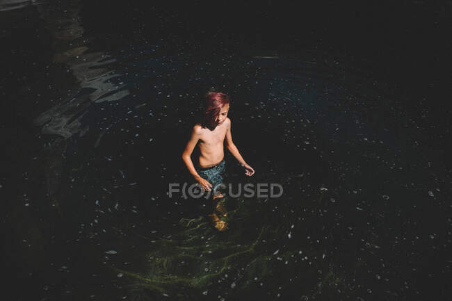 Tween menino com cabelos cor-de-rosa fica em um redemoinho de água escura — Fotografia de Stock