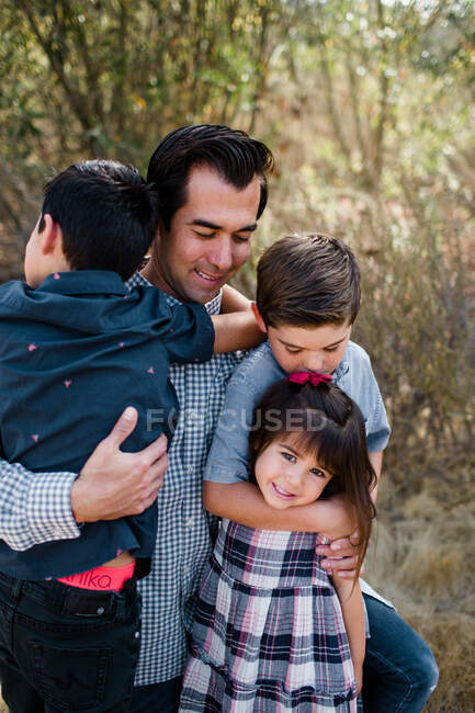 Papá sosteniendo a tres niños en el campo en San Diego - foto de stock