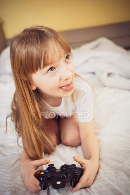 Mädchen spielt mit einer Konsole auf dem Bett — Stockfoto