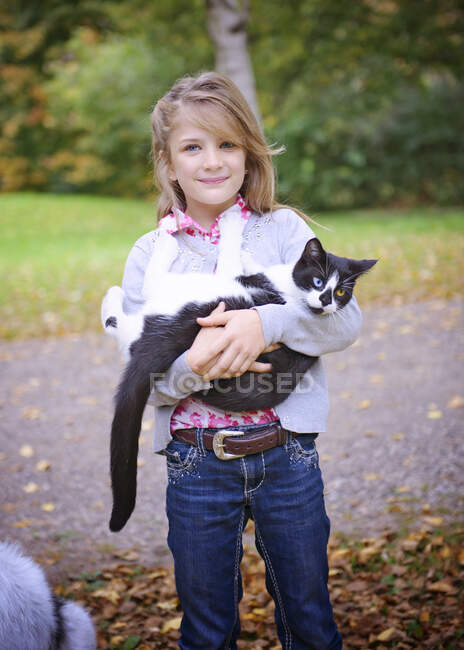 Jeune fille blonde tenant un chat noir et blanc à l'extérieur — Photo de stock