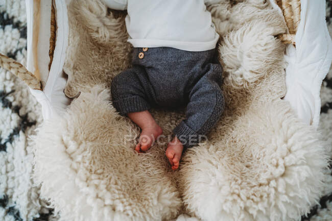 Vista dall'alto dei piedi del neonato nel cestino con tappeto di pelle di pecora — Foto stock