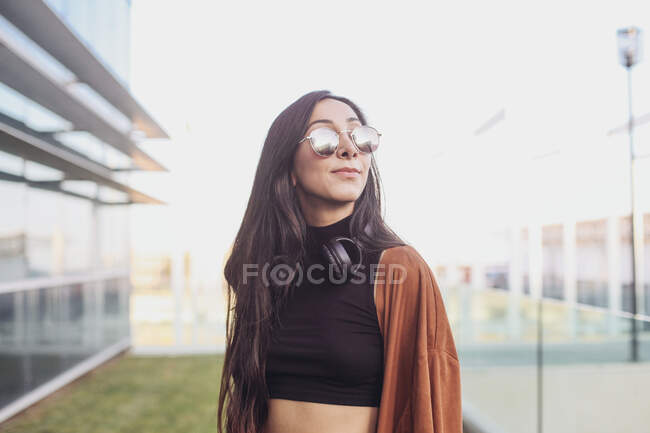 A young beautiful woman with long curly hair in a black dress and a white t-shirt and sunglasses — Stock Photo