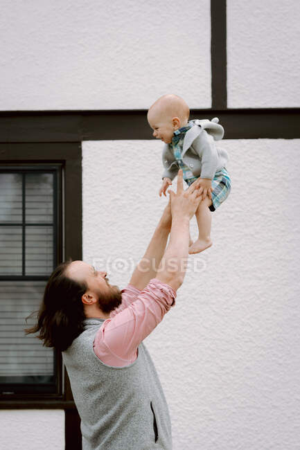 Веселый папа бросает смеющегося ребенка перед домом весной — стоковое фото