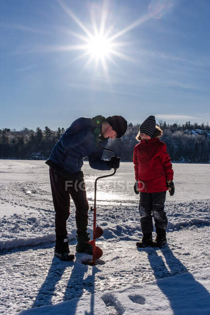 Два мальчика используют шнек, чтобы проделать дыру во льду в солнечный зимний день.. — стоковое фото