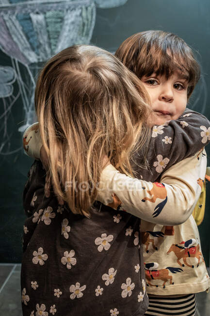 Los niños se abrazan en clase cariñosamente con una pizarra en t - foto de stock