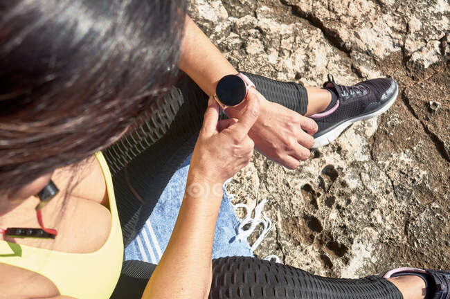 Latin woman, middle-aged, looking at app, smart watch, resting after gym session, wearing yellow top, black leggings, dumbbell, burning calories, staying fit, outdoors by the sea, blue sky, b — Stock Photo