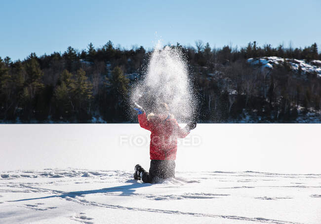 Young boy throwing snow in the air in the middle of a frozen lake. — Stock Photo