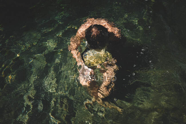 Ragazzo porta una pietra sommersa sotto l'acqua increspata — Foto stock