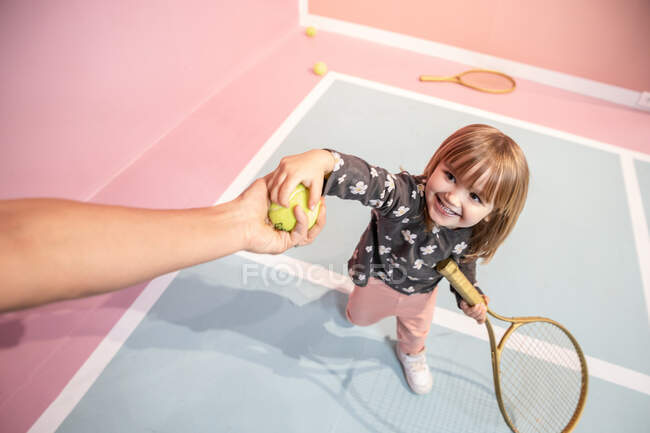 Kleines Mädchen, das Spaß hat und Tennis spielt, während jemand eine Tenni gibt — Stockfoto