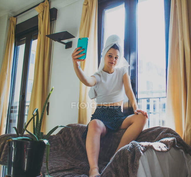 Jovem garota tirando foto de telefone celular enquanto sentado na cama na hora da manhã — Fotografia de Stock