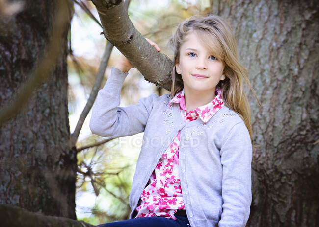 Jovencita rubia afuera sentada en un árbol. - foto de stock