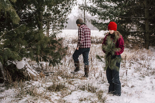 Garçon et fille dans un champ enneigé ramassant des branches de pin — Photo de stock