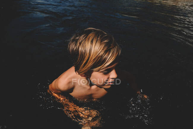 Niño emerge del agua negra en el sol de California - foto de stock