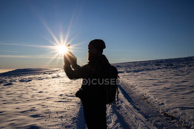Hombre trekking en tomar fotos en invierno puesta de sol - foto de stock