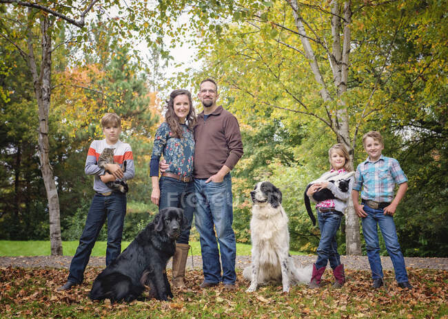 Familia feliz de cinco con perros y gatos por un camino rural. - foto de stock