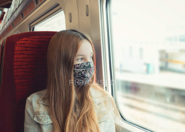 Молодой подросток путешествует на поезде в маске, выглядывая в окно — стоковое фото