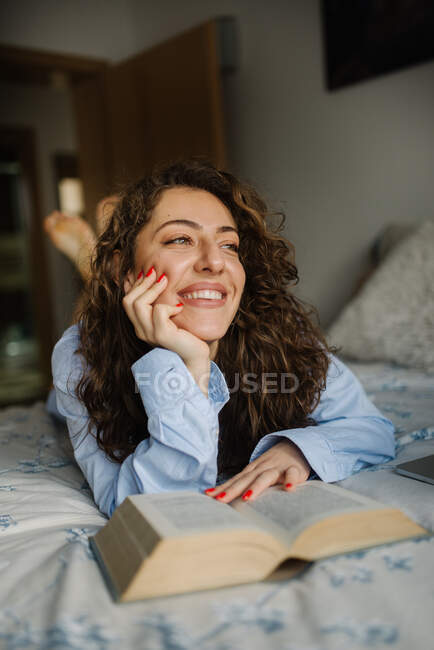 Щаслива молода жінка ремонтує книгу, що лежить в ліжку . — стокове фото