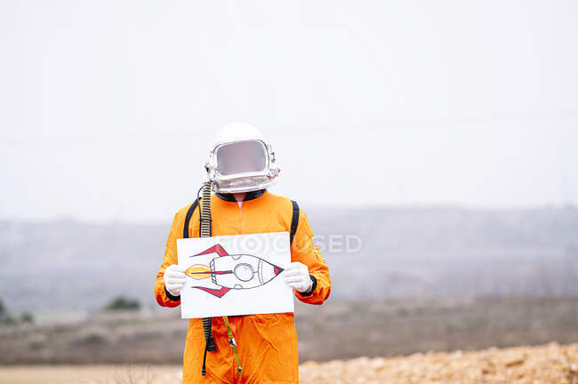 Homem vestido de astronauta segura um cartaz com um desenho de um foguete — Fotografia de Stock