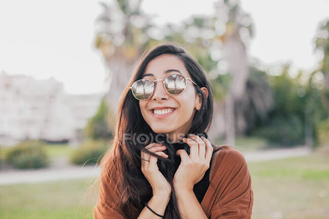 Молода красива жінка з довгим кучерявим волоссям у чорній сукні та білою футболкою та сонцезахисними окулярами — стокове фото
