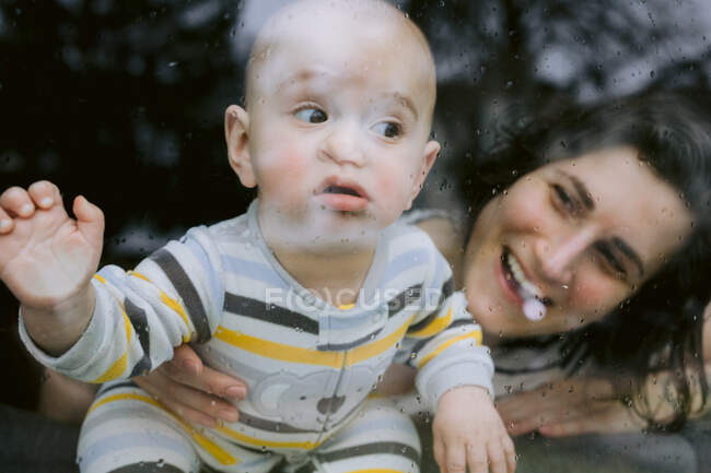 Lustiges Baby und Mama am verregneten Fenster während der Quarantäne — Stockfoto
