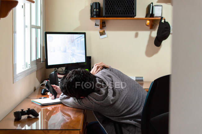 Hombre aburrido usando un teléfono en una habitación llena de tecnología durante un largo día - foto de stock