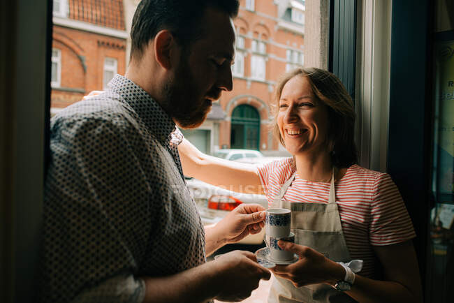 Супружеская пара, стоящая у входа с чашками кофе, улыбаясь — стоковое фото