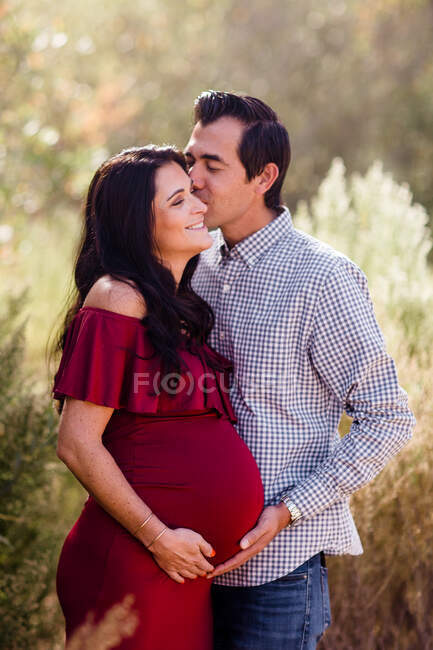 Marido beijando esposa expectante em campo em San Diego — Fotografia de Stock